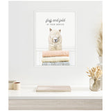 Framed canvas on a white wall depicting a fluffy alpaca head above neatly folded pastel towels with the text 'fluff and fold at your service' in gray script.