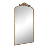 Tall rectangular mirror with an arched top and ornate carved wood detail in a warm brown finish at the crown.