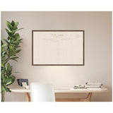 Large beige fabric pinboard framed in wood, printed with vintage postcard back design, hanging above a wooden desk with stacked books and a potted plant on the side.