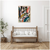 Abstract botanical artwork with bold, overlapping leaves in muted blues, greens, yellows, and pinks framed above a wooden bench with white cushions in a bright, minimalist room.