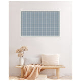 Light blue plaid fabric pinboard framed in white, hanging on a soft beige wall above a wooden bench with light neutral cushions and a beige throw, beside a white textured vase with dried flowers.