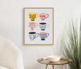 Framed art print featuring six colorful coffee cups with different floral patterns arranged in two columns on a white wall above a round gold table and white chair.