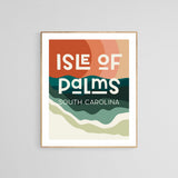 Framed modern art print with abstract layered waves in warm orange and green tones, featuring text 'Isle of Palms South Carolina' in bold, blocky letters.