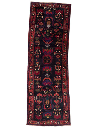 Hand-knotted Persian Hamadan tribal wool runner rug laid out on hardwood floor showing bold geometric and tribal motifs in earthy colors.