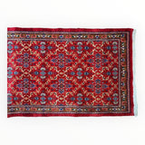 Rectangular vintage Mashhad wool runner with dense red field, intricate floral medallion motifs, and multicolored borders with white fringe on one short side.