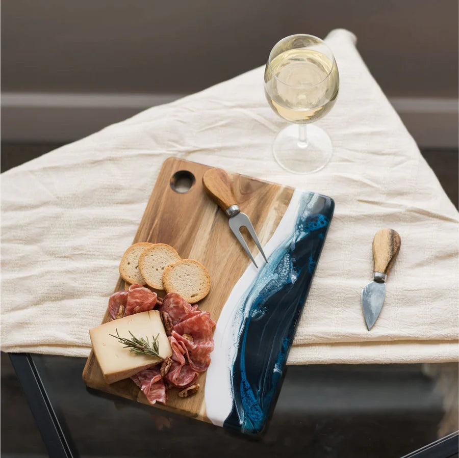Wooden Cheese Charcuterie Serving Board with cured meats, cheese, and bread on a white cloth with a glass of white wine.