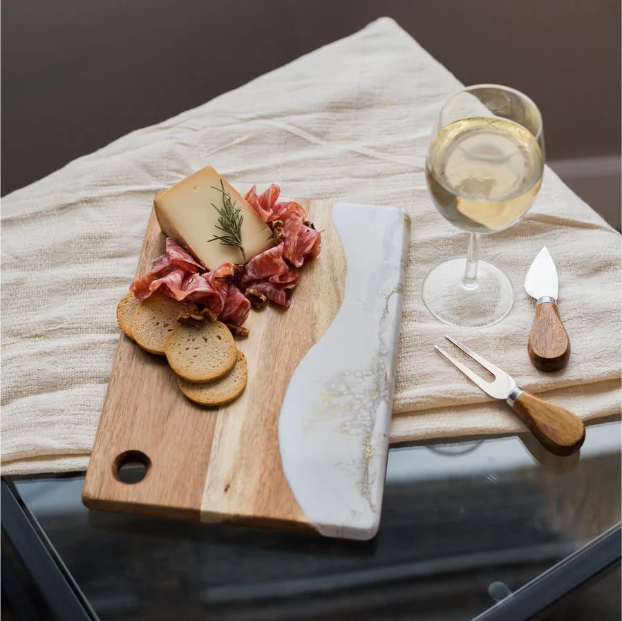 Wooden Cheese Charcuterie Serving Board with cured meats, bread, and a glass of white wine on a textured surface.