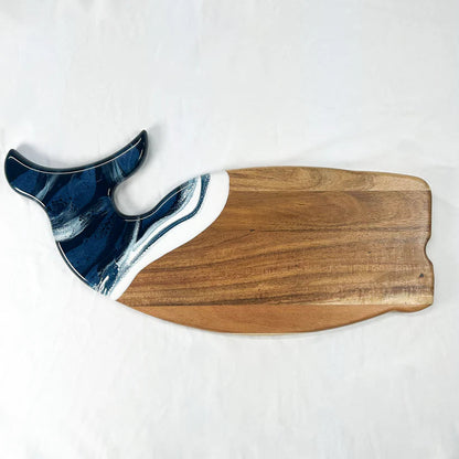 Wooden whale shaped charcuterie board with blue and white decorative element on a white background