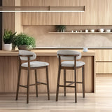 Two mid-century modern bar stools with curved beige upholstered seats and dark wood frames, positioned in a light wood kitchen with minimalist decor.