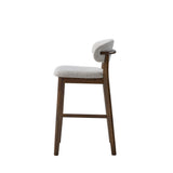 Side view of a mid-century modern bar stool with dark wood legs and frame, featuring a curved backrest and a cushioned seat upholstered in textured light gray fabric.