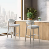 Two light wood mid-century modern bar stools with curved backrests and cushioned white fabric seats, positioned on a polished floor near a wood-paneled counter with plants and coffee cups.