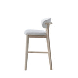 Side view of a mid-century modern bar stool with light wood legs and frame, featuring a curved upholstered seat and backrest in soft white textured fabric.