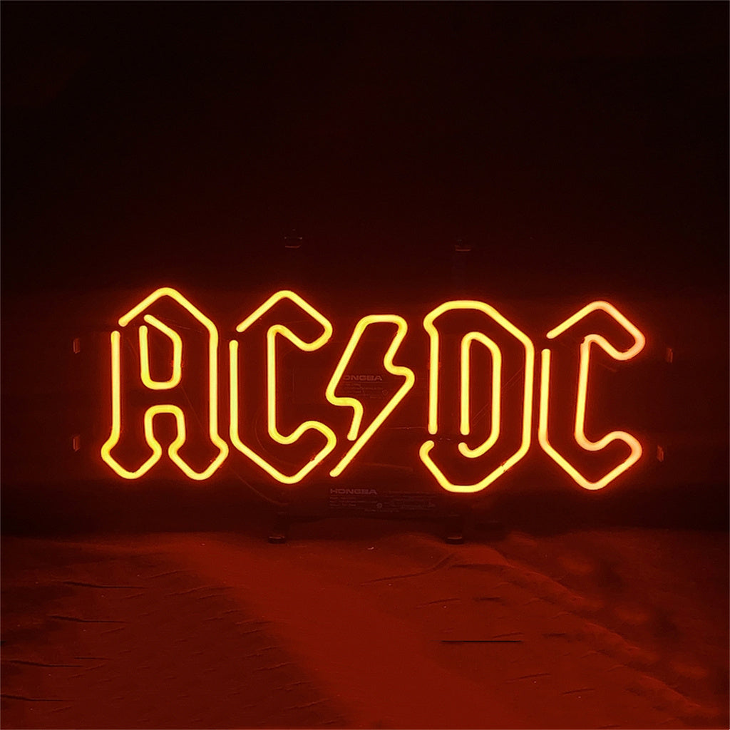 AD DC Neon Signs glowing with vibrant blue and pink neon illumination on a metal grid backing.