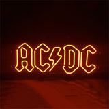 AD DC Neon Signs glowing with vibrant blue and pink neon illumination on a metal grid backing.