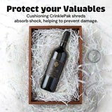 Bottle of wine cushioned within a wooden box filled with white iridescent crinkle paper shreds on a marble surface, accompanied by curled paper strips outside the box.