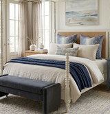 Bed with cream duvet and navy blue textured throw, navy blue antelope-pattern pillows, beige headboard, and abstract seascape painting on white wall.