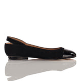 Black slingback flat shoe with matte suede body and glossy patent toe cap, shown in side profile on reflective surface