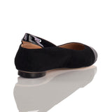 Black suede flat shoe with shiny black patent leather toe cap and heel detail, shown from a rear side view on a reflective surface.