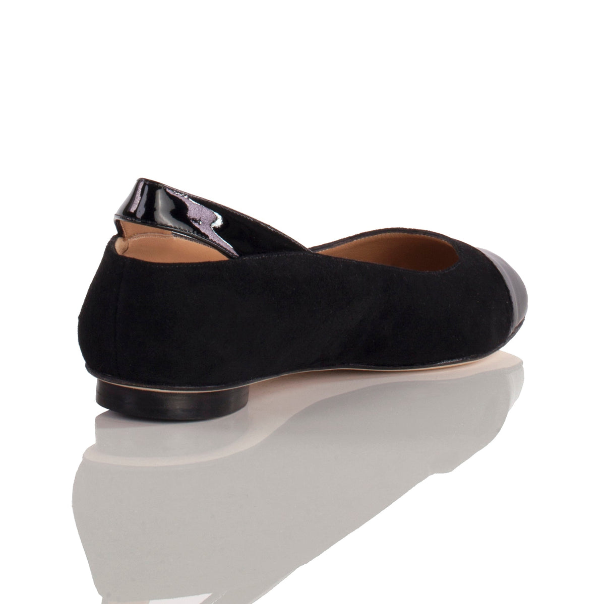 Black suede flat shoe with shiny black patent leather toe cap and heel detail, shown from a rear side view on a reflective surface.