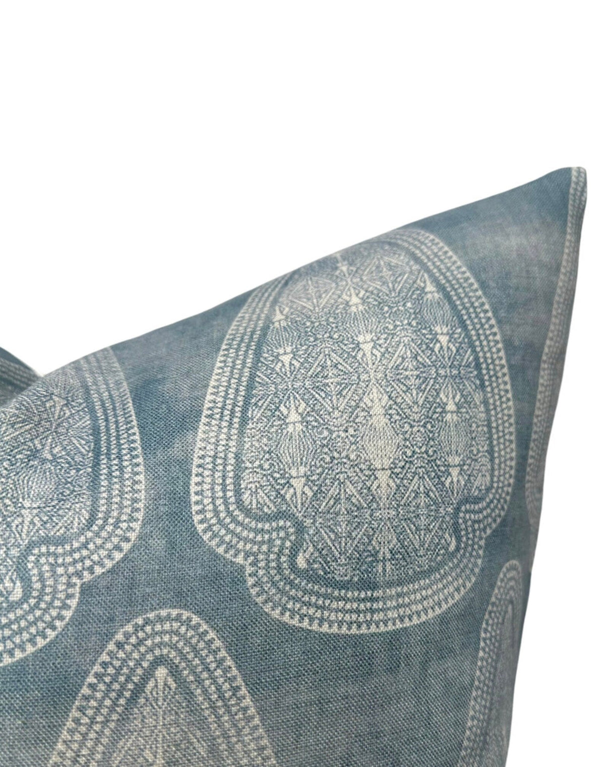 Close-up of a lake blue pillow cover with large, symmetrical white geometric and floral patterns and a distressed textured fabric appearance.