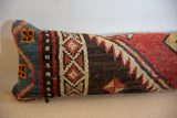 Elongated lumbar pillow featuring geometric and diamond patterns with colors including teal, rust, cream, black, and mustard on a textured fabric.