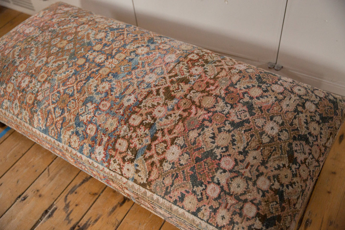 Rectangular ottoman upholstered with a vintage Persian rug featuring intricate floral and geometric patterns in muted reds, blues, and beige tones, set on a wooden floor.