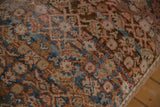 Close-up of a vintage Persian rug with intricate floral patterns in muted blue, brown, and beige tones, showing textured woven fabric.