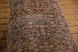 Close-up of a vintage Persian rug with intricate floral and geometric patterns in muted blue, rust, and beige tones on a wooden floor background.
