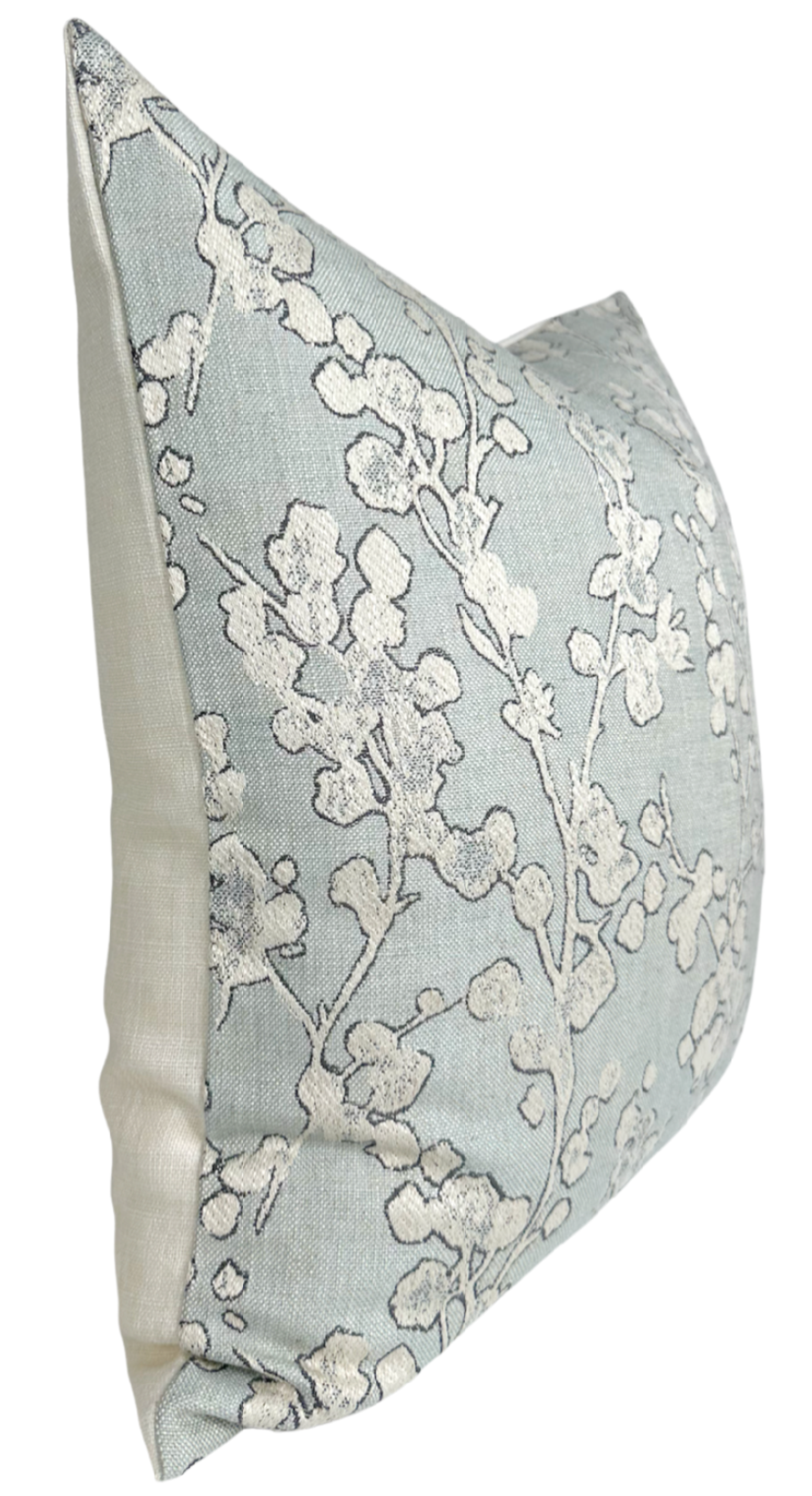 Light blue pillow cover with white and gray floral branch pattern on front and beige solid fabric on back, shown angled from the side.