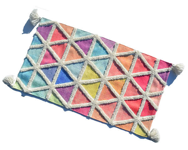 Multi color accent rug with diamond pattern and four corner fringes laid on floor