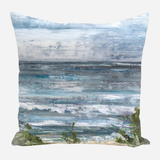 Square pillow featuring an abstract seascape with horizontal brushstrokes in shades of blue, gray, and white, and green accents at the bottom suggesting foliage.