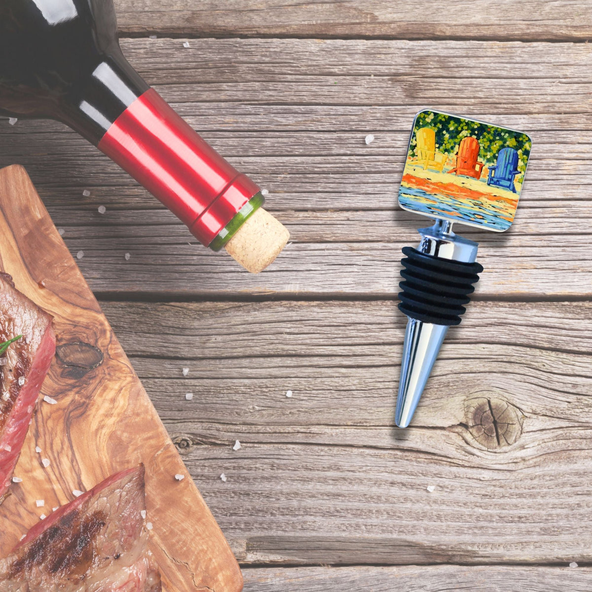 Metal wine bottle stopper with a square top depicting colorful Adirondack chairs on a beach, shown on a weathered wooden surface next to a wine bottle and cutting board.