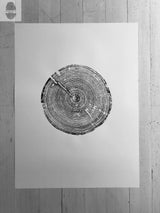 Black and white print of tree rings on a white sheet centered on a textured wooden surface, showing detailed tree growth patterns.