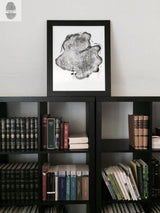 Black and white print of an Alaska cedar wood slice showing growth rings, framed in black and displayed on a black bookshelf filled with books.