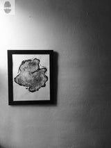 Black and white framed print of a wood slice with detailed annual rings, mounted on a textured light wall in a minimalist setting.
