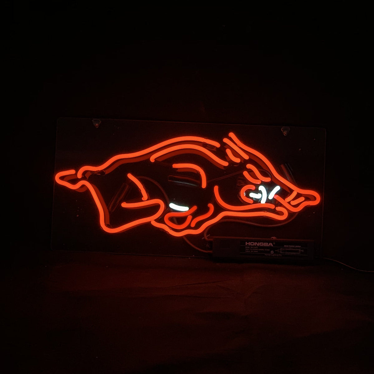 Red neon light shaped as a stylized wild hog with white neon accents depicting eyes and tusks on a black background.