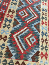 Close-up of an Afghani Maimana Kilim rug featuring geometric diamond motifs in red, blue, cream, and brown with patterned borders of smaller repeating shapes.