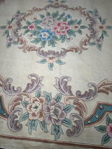Hand-tufted Chinese Aubusson wool rug with floral medallions in pastel pink, blue, and green on a beige background and ornate scroll patterns.