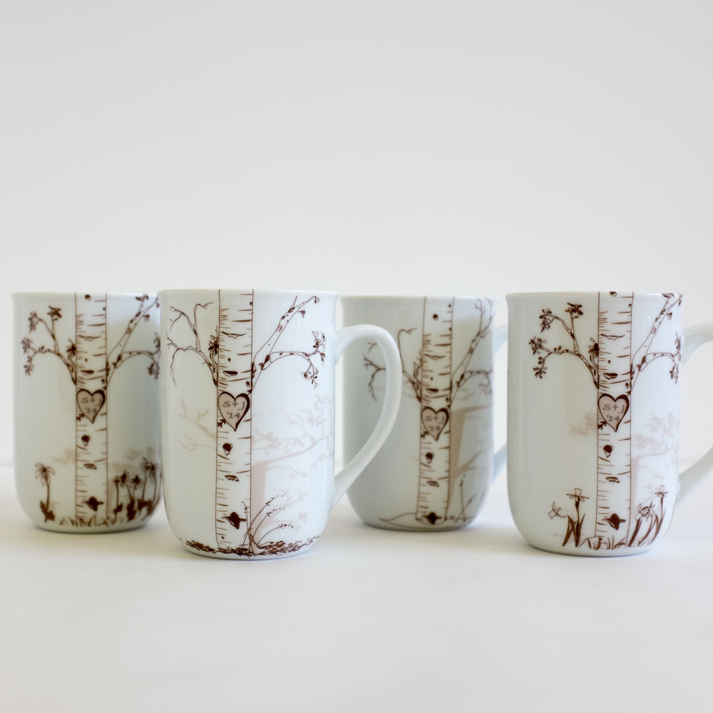 Four white ceramic mugs with brown birch tree illustrations, each featuring carved heart designs with custom initials inside, displayed on a white surface.
