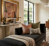 Black velvet chaise lounge with three decorative pillows in rust, olive, and geometric patterns, placed next to a marble console with abstract sculpture and framed artwork.