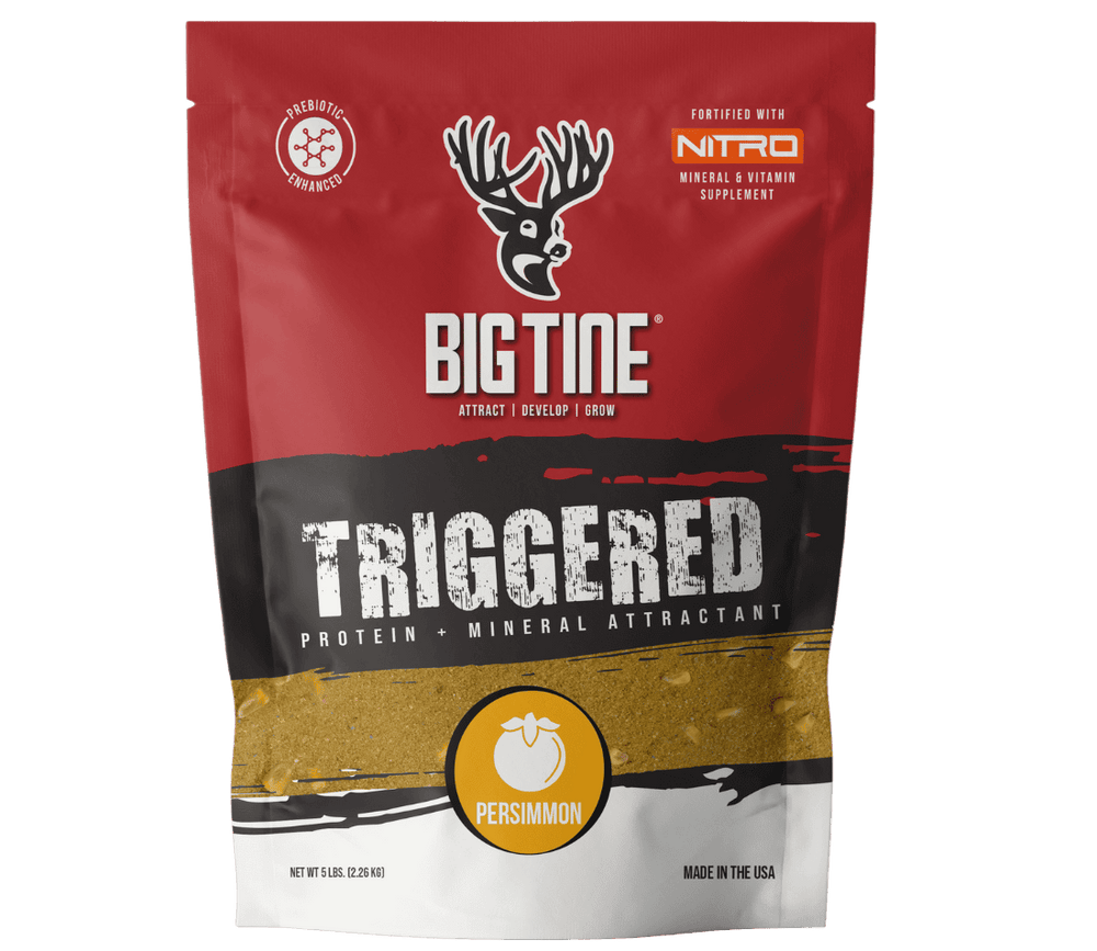 Red and black Big Tine Triggered Persimmon attractant bag featuring a white deer head logo and orange persimmon icon, standing upright against a green background