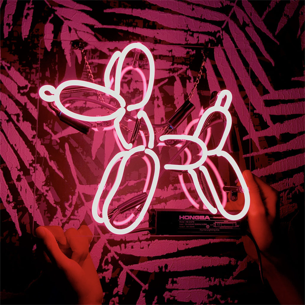 Pink neon light shaped like a balloon dog being held by two hands against a patterned dark red and black wall.