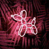 Bright pink neon light shaped like a balloon dog mounted on a wall with dark fern leaf patterns and brick texture in the background.