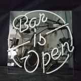 White neon sign reading 'Bar is Open' within a circular border, mounted on a reflective black backing, showing electrical components and wires.