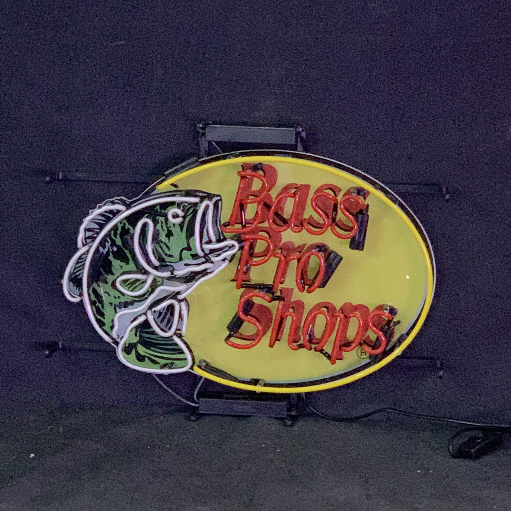 Oval neon sign with yellow background featuring a green bass fish outline and red 'Bass Pro Shops' text in the center, mounted on a black frame.