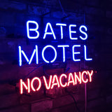 Neon sign with blue text 'BATES MOTEL' above red text 'NO VACANCY' mounted on a dark brick wall and lit in dim lighting.