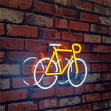 Yellow and white neon bicycle sign hanging on a rustic red brick wall, with clear plastic backing and a black electrical cord.