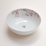 White ceramic bowl with brown botanical illustrations and a small heart shape inside, viewed from above against a white background.