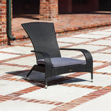 Black woven wicker lounge chair with curved arms and a gray seat cushion, positioned on a patterned brick and concrete patio outdoors.