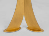 Close-up of two curved gold metal legs with flat oval bases positioned side by side against a plain light background.